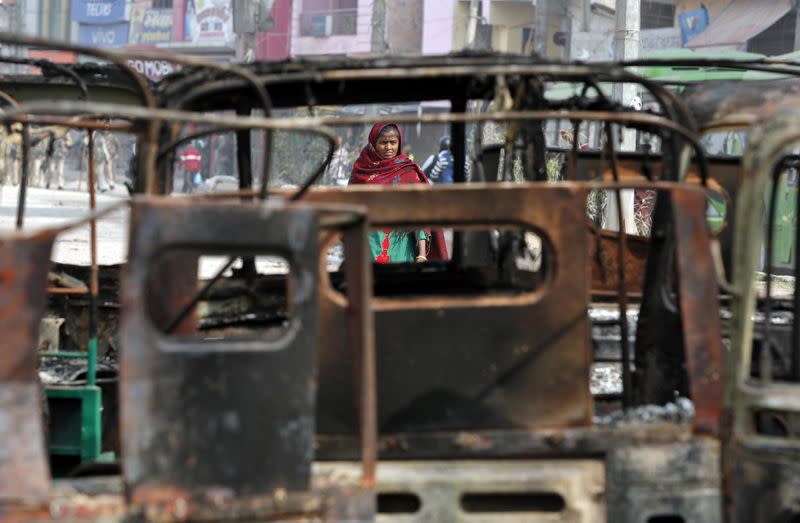 A woman walks past charred vehicles in a riot affected area following clashes between people demonstrating for and against a new citizenship law in New Delhi