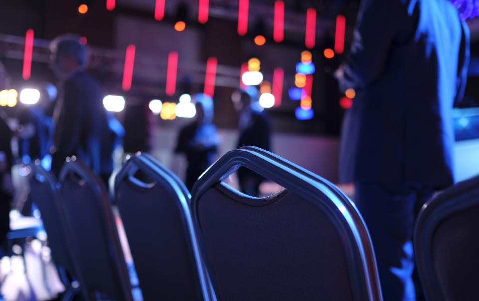 Back view of professionals in a conference room with empty chairs and blurred colorful lights in the background