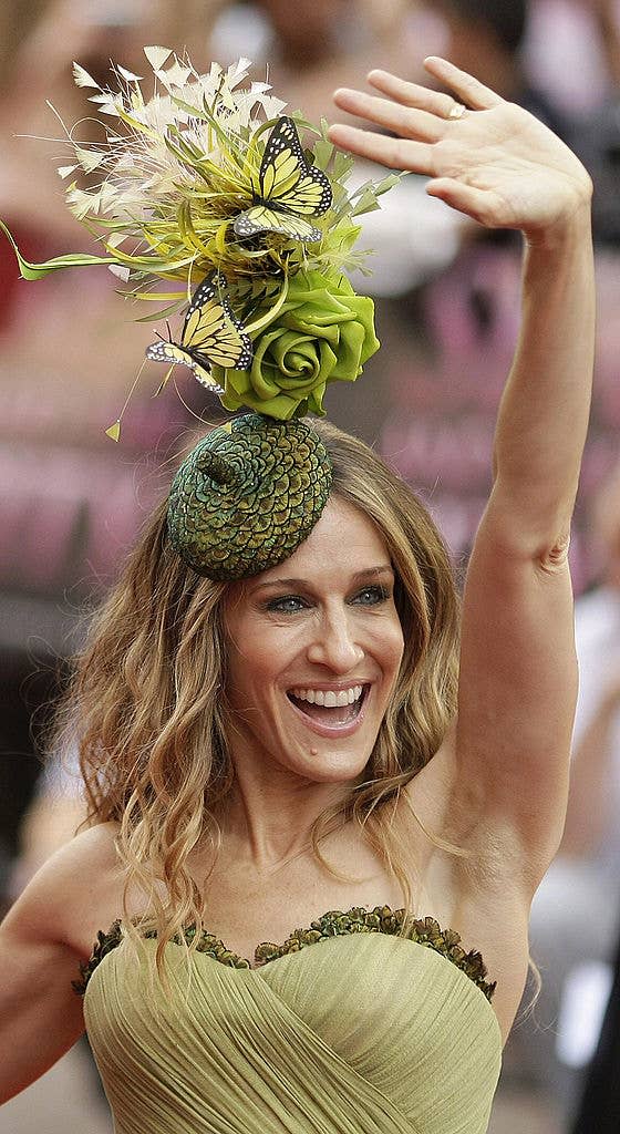 Sarah Jessica Parker waves, wearing a detailed green and yellow headpiece with a butterfly, and a green strapless dress at a public event