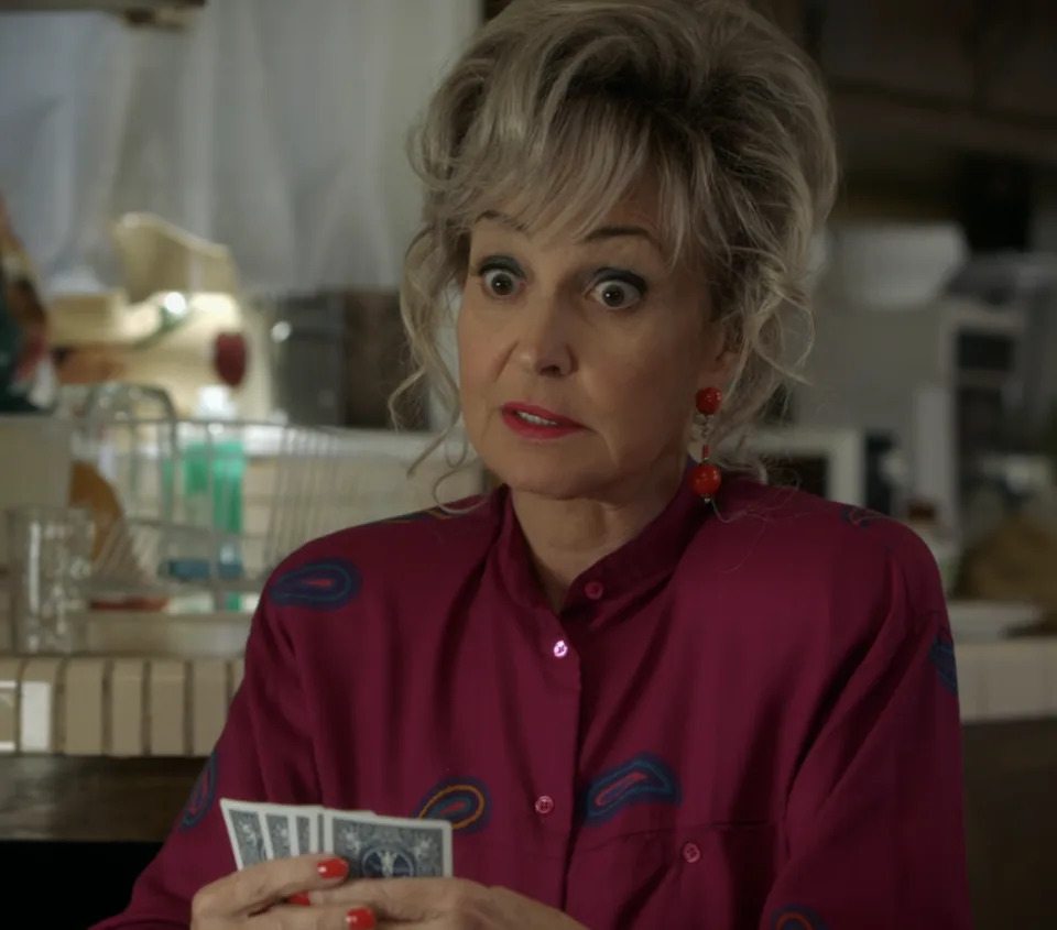 Connie with expressive eyes, holding cards, dressed in retro-style blouse with earrings