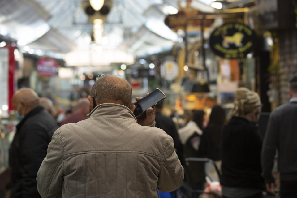 A man speaks on his mobile phone in the Mahane Yehuda market in Jerusalem, Wednesday, Dec. 23, 2020. In the early days of the pandemic, a panicked Israel began using a mass surveillance tool on its own people, tracking civilians’ mobile phones to halt the spread of the coronavirus. But months later, the tool’s effectiveness is being called into question and critics say its use has come at an immeasurable cost to the country’s democratic principles. (AP Photo/Maya Alleruzzo)