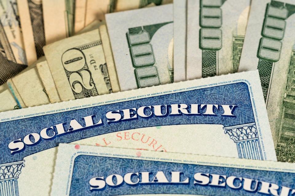 Two Social Security cards sitting atop a pile of fanned-out U.S. currency.