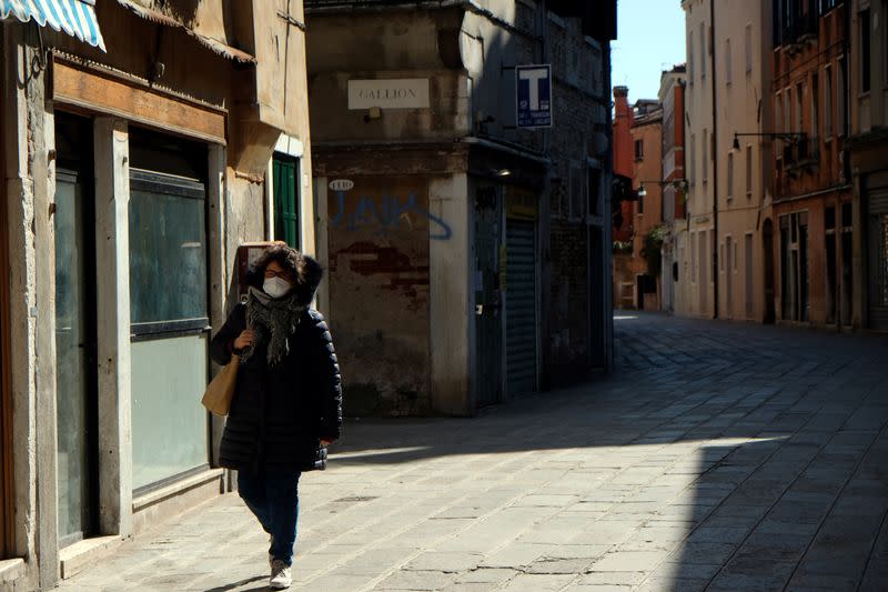 A woman wearing a protective mask in an empty street of Venice on Sunday with an unprecedented lockdown across of all Italy imposed to slow the outbreak of coronavirus, in Venice