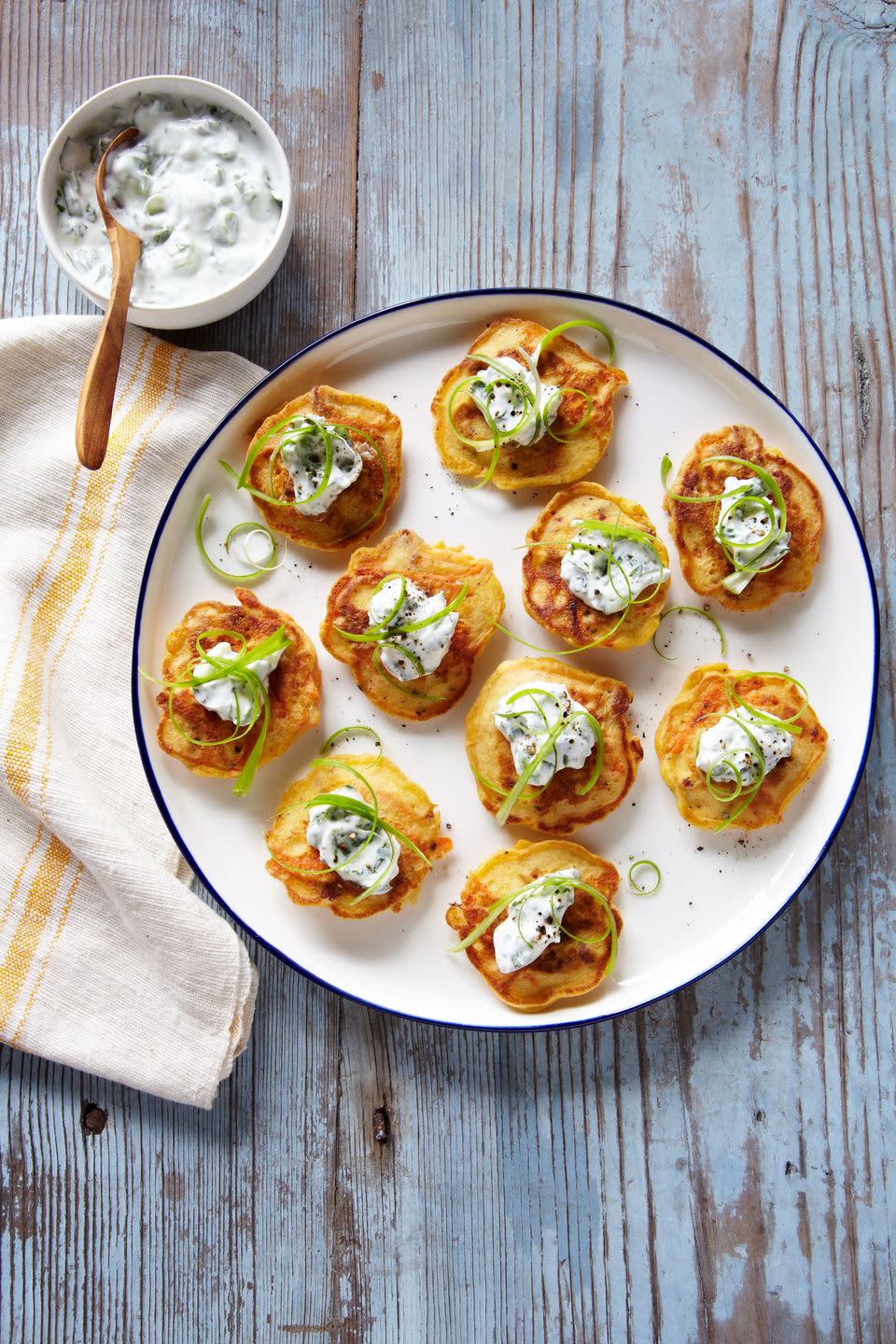 carrot chorizo blinis arranged on a white plate and topped with a yogurt topping and garnished with scallions