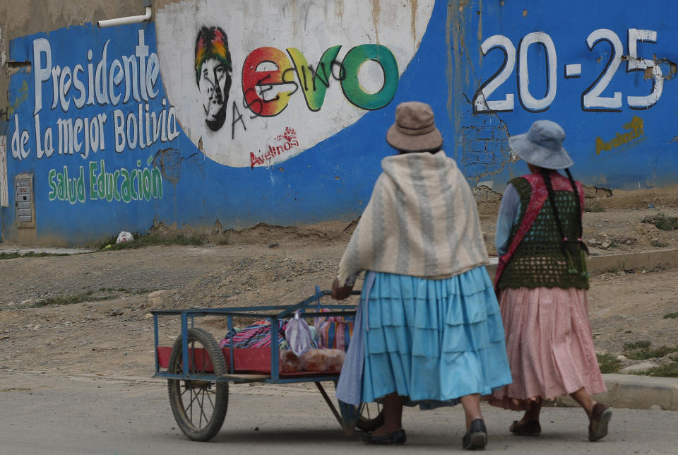 En esta imagen del 18 de enero de 2020, mujeres pasando junto a un mural que pedía la reelección del expresidente de Bolivia, Evo Morales, en El Alto, Bolivia. In this Jan. 18, 2020 photo, women walk past a mural promoting the re-election of Bolivia's former President Evo Morales, in El Alto, Bolivia. “La imagen de Morales no es casual, estaba enfocada para sostener el régimen caudillista que se impulsó desde su partido de gobierno”, dijo a The Associated Press la analista política y socióloga María Teresa Zegada, quien agregó que cualquier nuevo gobernante tomaría una decisión como la de Áñez para dejar atrás al gobernante que le precedió. (AP Foto/Juan Karita)