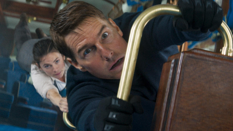 Hayley Atwell hangs onto Tom Cruise as he hangs onto a railing in Mission Impossible: Dead Reckoning - Part One.