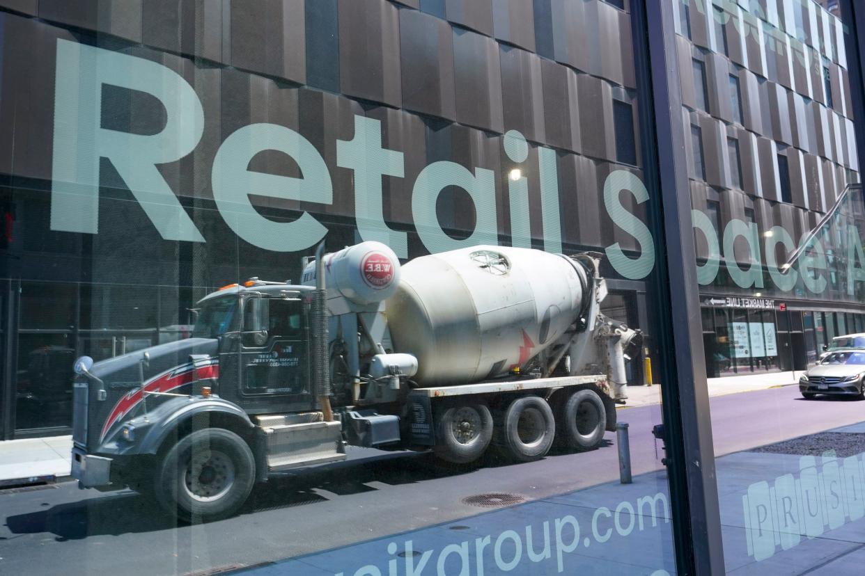 A cement mixer truck is reflected on a window of window advertising retail space for rent at a residential and commercial building under construction at the Essex Crossing development on the Lower East Side on Thursday.