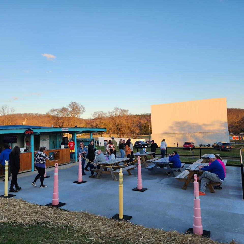 People walk around and sit on picnic benches in Hull's Drive In Theater. 