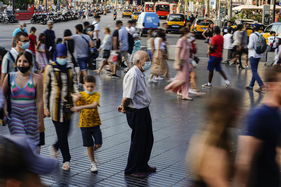 FILE - A man wearing a face mask to protect against the spread of coronavirus pauses as people walk along a street in downtown Barcelona, Spain, July 3, 2021. The Spanish government on Tuesday, July 4, 2023, declared an end to the health crisis caused by the COVID-19 pandemic, and says people no longer have to wear masks in health and care centers as well as pharmacies. (AP Photo/Joan Mateu, File)