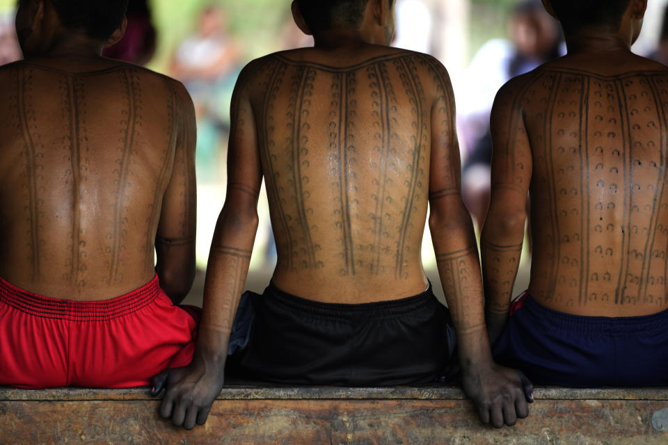 Boys with traditional paintings made of Jenipapo ink, a traditional Indigenous body paint, sit on a bench on the dawn of the second day of the Wyra'whaw coming-of-age festival in the Ramada ritual center, in Tenetehar Wa Tembe village, located in the Alto Rio Guama Indigenous territory in Para state, Brazil, Saturday, June 10, 2023. Known as the Menina Moca in Portuguese, the three-day festival is for adolescent boys and girls in Brazil's Amazon. (AP Photo/Eraldo Peres)