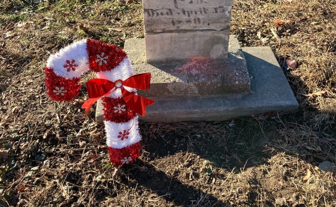 A candy cane decoration has been placed by a gravestone at Honey Creek Cemetery in West Allis.