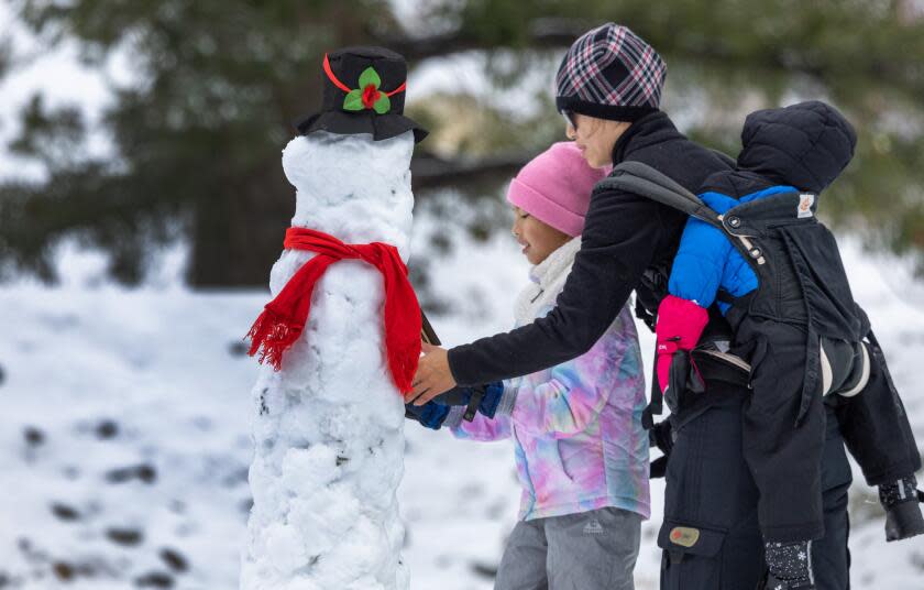 Mt. Baldy, CA - January 03: Amelia Dinh, 7, left, and mom Mai Dinh, right, put the finishing touches on a snowman along Mt. Baldy Rd. on Wednesday, Jan. 3, 2024 in Mt. Baldy, CA. (Brian van der Brug / Los Angeles Times)