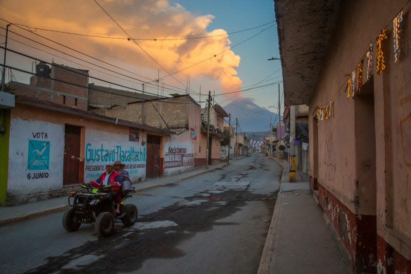 Residents ride a quad while in the background the volcano Popocatepetl emits ash, steam and gas in Mexico.