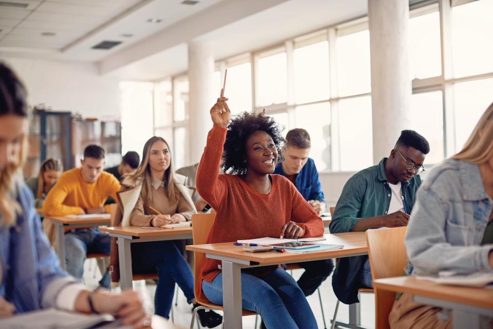 A student raises her hand to ask a question during a classroom lecture.