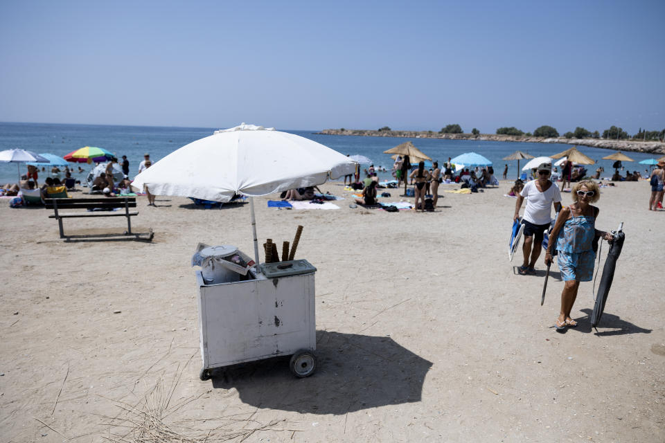 Swimmers carry their belongings as they leave a beach at Glyfada suburb, in Athens, Greece, Saturday, July 15, 2023. Temperatures reached up to 42 degrees Celsius in some parts of the country, amid a heat wave that continues to grip southern Europe. (AP Photo/Yorgos Karahalis)