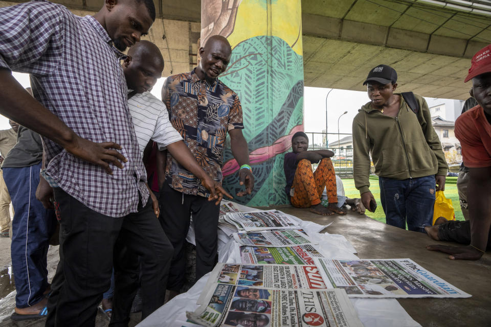 People discuss Saturday's election as they look at newspapers from a street vendor at an intersection in Lagos, Nigeria on Sunday, Feb. 26, 2023. Nigerians voted Saturday to choose a new president, following the second and final term of incumbent Muhammadu Buhari. (AP Photo/Ben Curtis)