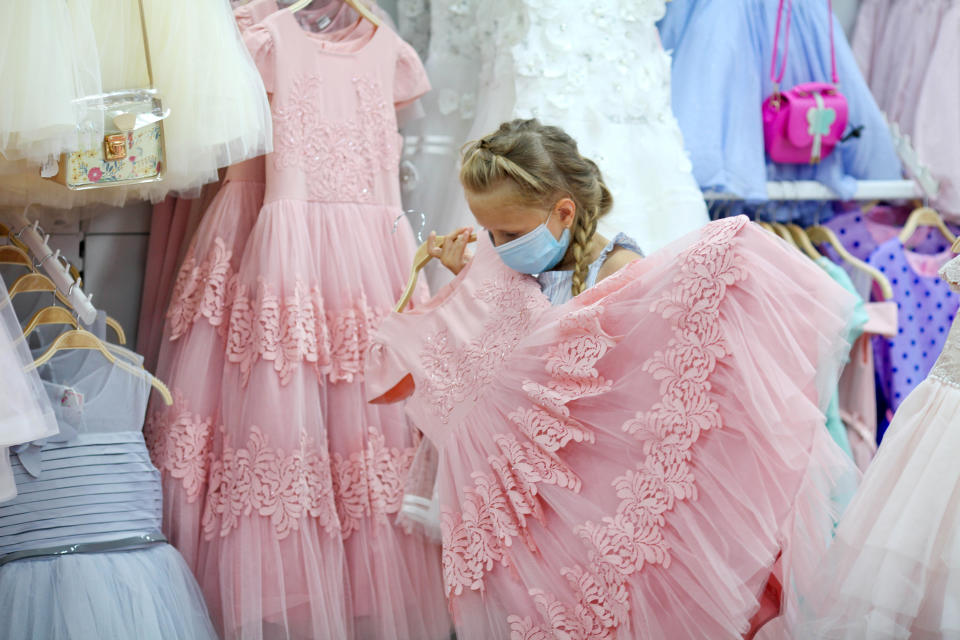 Child with Covid-19 safety measures buys beautiful pink dress, social distancing. Girl in the store chooses a dress for a holiday