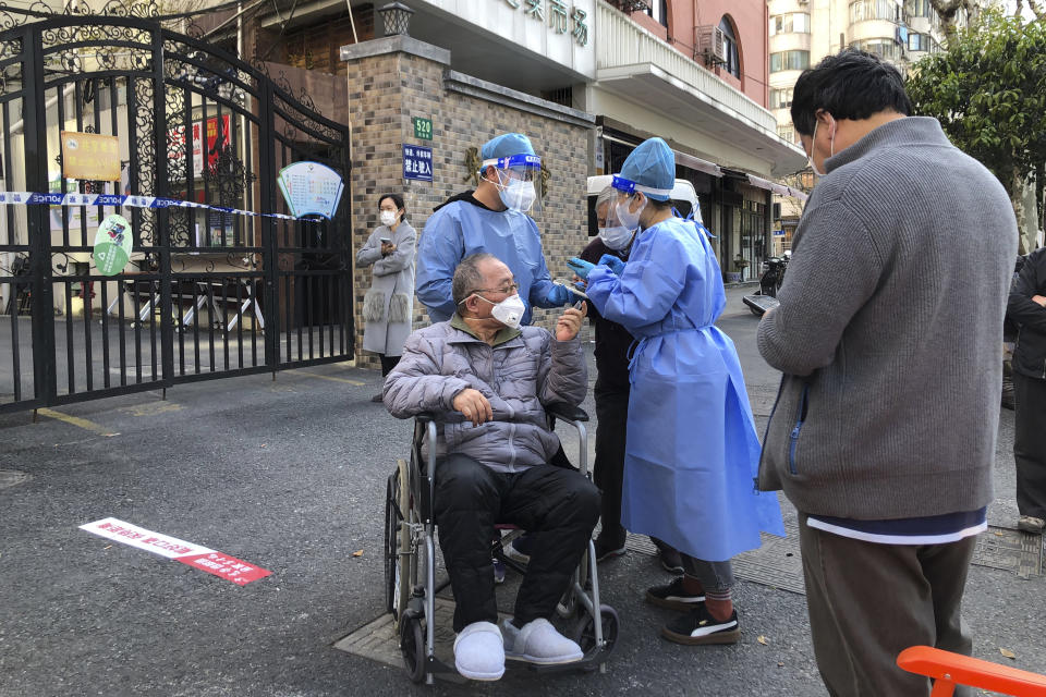 FILE - Workers in protective gear help a man in a wheelchair during the mass testing for residents in a lockdown area in the Jingan district of western Shanghai on April 4, 2022. Shanghai's lockdown is an abrupt about-face from just a month ago, when some Chinese health experts publicly suggested softening pandemic control measures. (AP Photo/Chen Si, File)