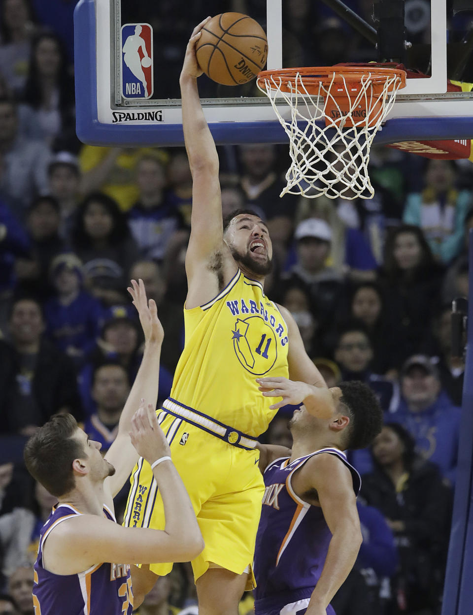 Golden State Warriors guard Klay Thompson (11) dunks over Phoenix Suns forward Dragan Bender, left, and guard Devin Booker during the first half of an NBA basketball game in Oakland, Calif., Sunday, March 10, 2019. (AP Photo/Jeff Chiu)
