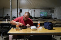 Josh Anderson, Minneapolis, Minn., an electrical worker for Sparks Energy, eats a dinner in a cafeteria of a tent city for electrical workers, in Amelia, La., Thursday, Sept. 16, 2021. In one massive white tent, hundreds of cots are spread out; experienced workers bring their own inflatable mattresses. Another tent houses a cafeteria that serves hot breakfast starting about 5 a.m., dinner and boxed lunches that can be eaten out in the field. (AP Photo/Gerald Herbert)