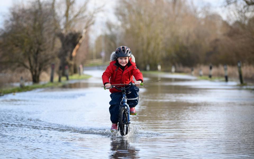 A child cycles along the flooded road by the side of the River Great Ouse - Leon Neal/Getty Images