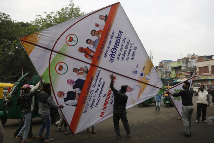 People carry a giant kite made to create awareness about COVID-19 in Ahmedabad, India, Thursday, Jan. 6, 2022. Coronavirus cases fueled by the highly transmissible omicron variant have rocketed through India and the country is scrambling to ward off its impact by swiftly introducing a string of restrictions that the population thought were history. But India's political leaders, including Modi, have largely flouted some of these guidelines and traversed cities in a massive campaign trail ahead of crucial state polls, addressing packed rallies of tens of thousands of people without masks. (AP Photo/Ajit Solanki)