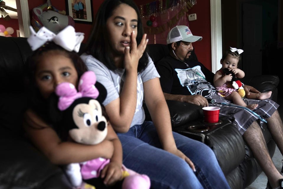 Freddy Fernandez holds his 8-month-old daughter, Mariana, as he sits with his fiancé, Vanessa Cruz, and their other daughter, Melanii, 4, in the living room of their home Friday, June 10, 2022, in Carthage, Mo. After contracting COVID-19 in August 2021, Fernandez spent months hooked up to a respirator and an ECMO machine before coming home in February 2022 to begin his long recovery from the disease. (AP Photo/Charlie Riedel)