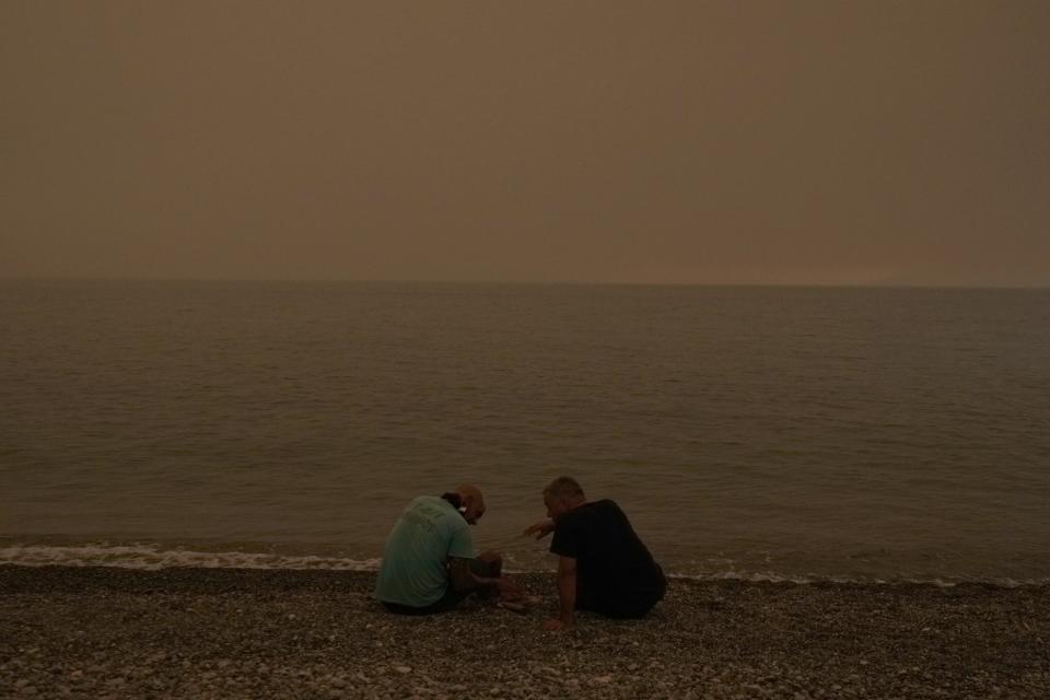 People gather on the beach during a wildfire at Pefki village on Evia island, about 189 kilometers (118 miles) north of Athens, Greece, Sunday, Aug. 8, 2021. Pillars of billowing smoke and ash are blocking out the sun above Greece's second-largest island as a days-old wildfire devours more pristine forests and triggers more evacuation alerts. (AP Photo/Petros Karadjias)