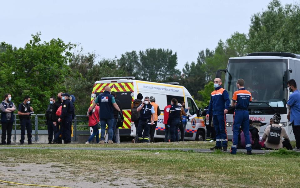 Migrants sit near a bus and a securite civile vehicle as police supervise the evacuation of a camp on the road to Saint-Omer near Calais, northern France - DENIS CHARLET 