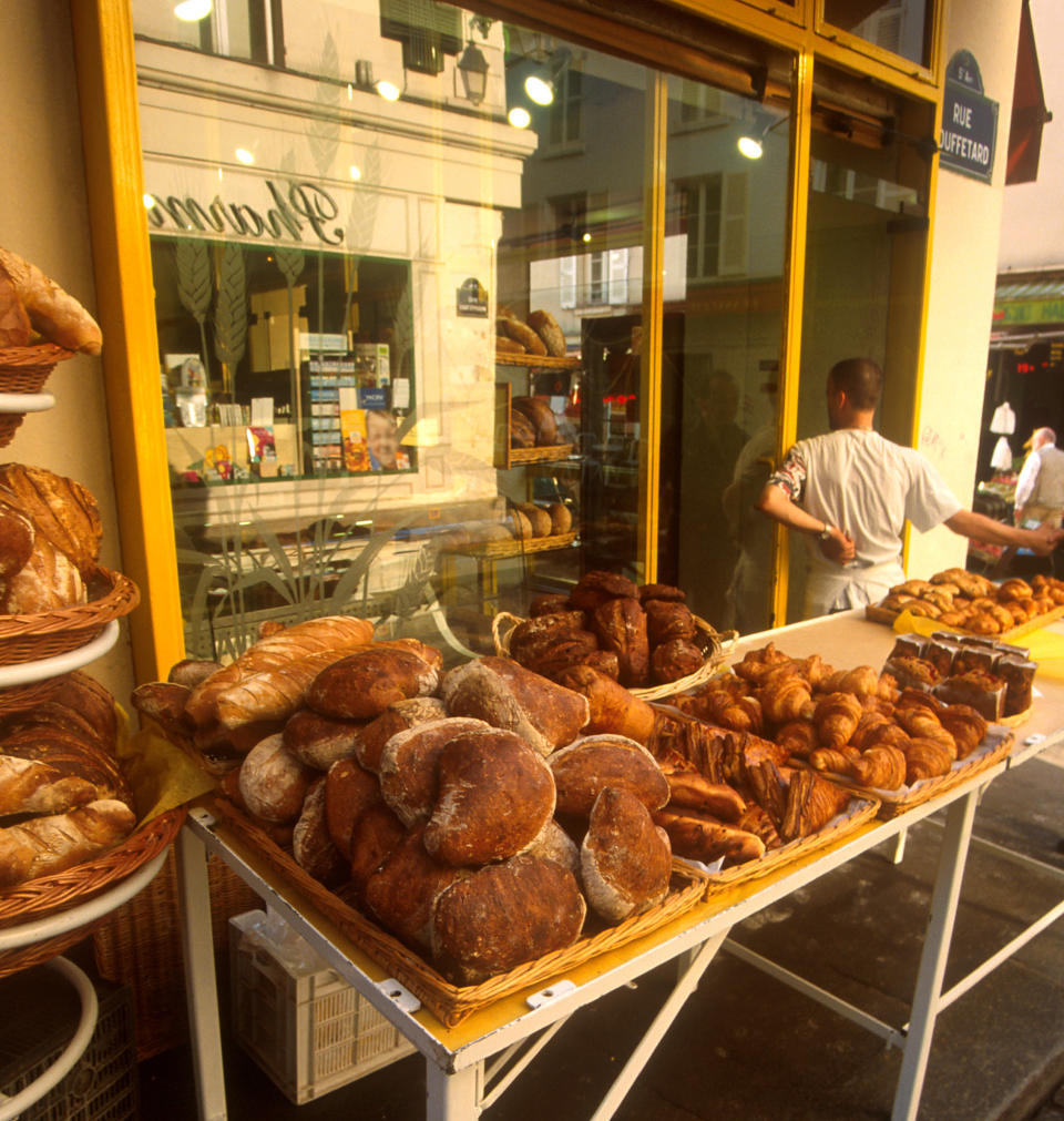 Bakery display with various breads and pastries on tables, a storefront in the background, and a person facing away