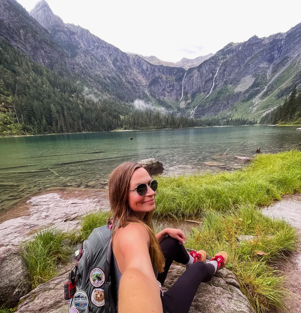 A woman taking a selfie in front of a lake and mountains.