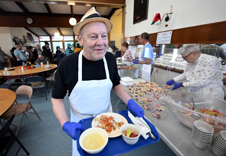 Soup Kitchen in Provincetown volunteer Chris Pula brings food on Dec. 29 to a seated guest who was unable to stand in line for the lunch. The dishes of the day were chicken egg drop soup, miso soup, kung pao chicken and tofu with rice and fresh fruit