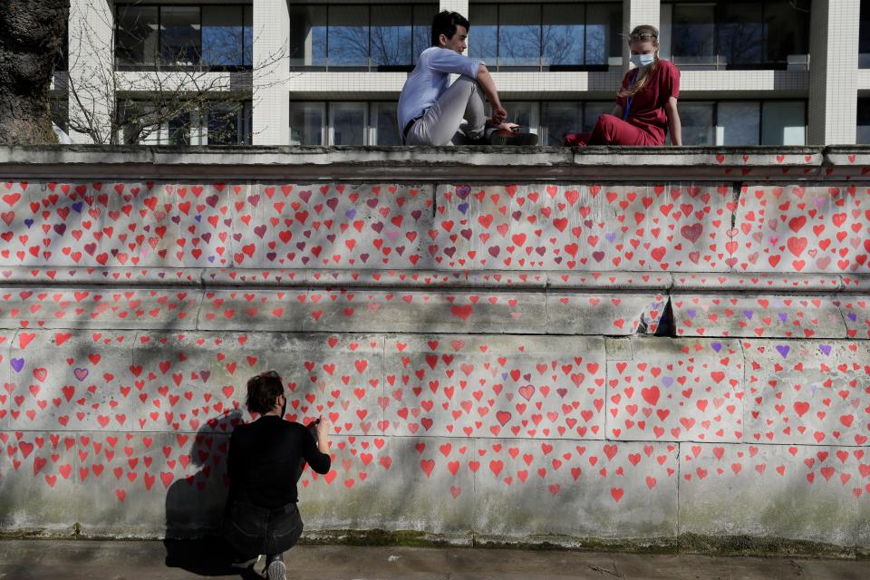 Hospital staff from St Thomas' Hospital watch from the top of the wall as members of bereaved families paint red hearts on the COVID-19 Memorial Wall opposite the Houses of Parliament on the Embankment in London, Monday March 29, 2021.