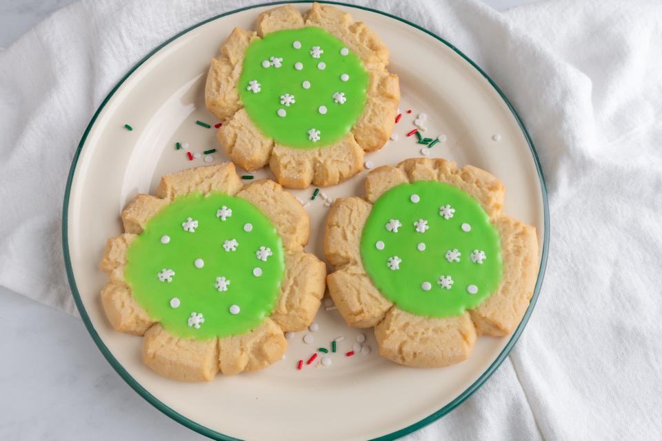 Flower-shaped cookies with green icing in the center and white sprinkles shaped like circles and snowflakes