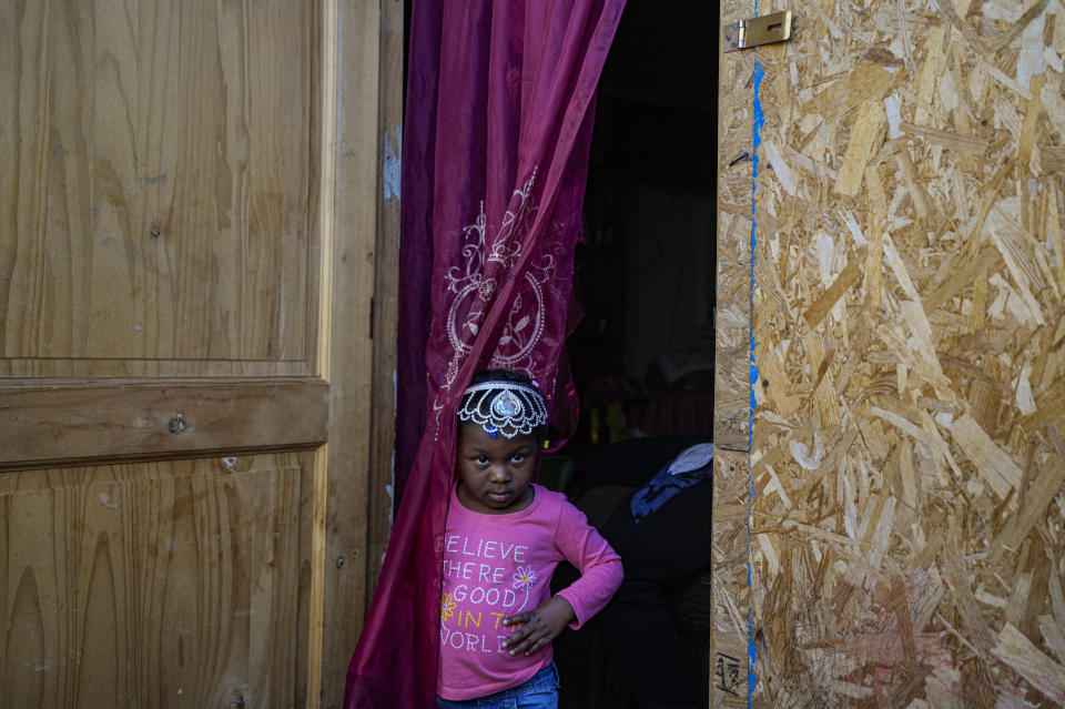 Chilean-born, three-year-old Benita, whose parents are Haitian, peers from her home's front door, in the Dignidad camp set up by migrants in Santiago, Chile, Thursday, Sept. 30, 2021. Benita's parents have not been able to renew their Chilean identity cards, which keeps them from being able to work legally. (AP Photo/Esteban Felix)