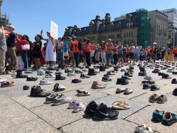 People and shoes line the ground in front of Parliament Hill in Ottawa, where a pair of NDP MPs have organized a march to call on the Canadian government to investigate crimes in residential schools. (Frederic Pepin/Radio-Canada - image credit)