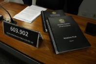 A plaque with the number of COVID-19 deaths in Brazil sits next to copies of a Senate commission report on the government's handling of the pandemic, at the Federal Senate in Brasilia, Brazil, Wednesday, Oct. 20, 2021. A senator formally presented the report recommending President Jair Bolsonaro be indicted on criminal charges for allegedly bungling Brazil's response to the COVID-19 pandemic and pushing the country's death toll to second-highest in the world. (AP Photo/Eraldo Peres)