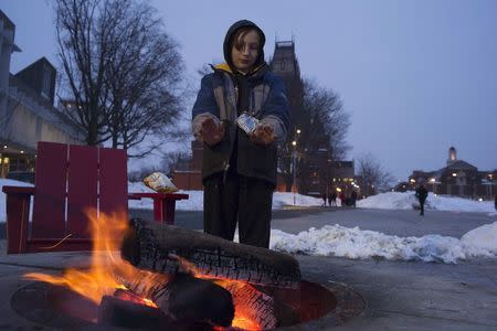 A boy warms his hands at a fire pit on cold winter evening outside the Science Center at Harvard University in Cambridge, Massachusetts February 18, 2015. REUTERS/Brian Snyder