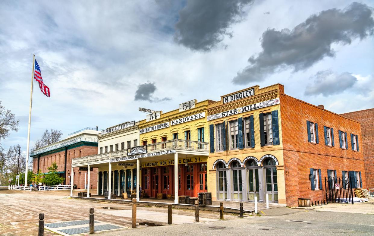 Buildings of Old Sacramento Historic District, Sacramento, California, an American flag on the left, a dramatic light blue sky with grey clouds