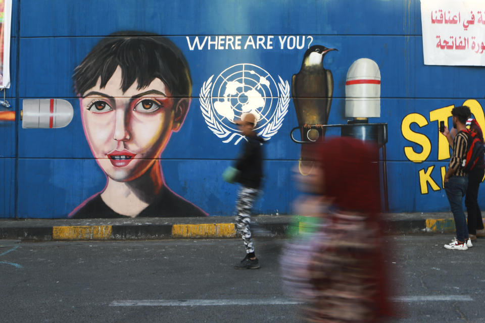 In this Sunday, Nov. 17, 2019 photo, taken with slow camera shutter speed, people pass by graffiti at the Saadoun tunnel, in Baghdad, Iraq. The tunnel that passes under Baghdad’s landmark Tahrir Square has become an ad hoc museum for Iraq's revolution: Young artists draw images and murals that illustrate the country’s tortured past, and the Iraq they aspire to. (AP Photo/Hadi Mizban)