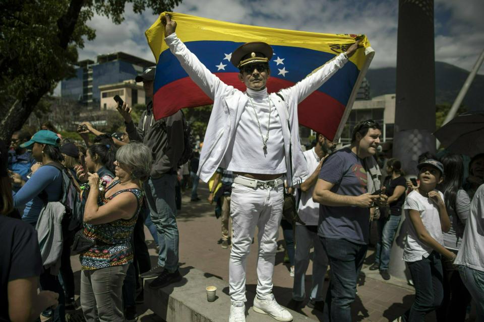 Jose Ramon Salas strikes a pose holding a Venezuelan national flag and wearing a Russian military cap at an opposition rally to propose amnesty laws for police and military, in Las Mercedes neighborhood of Caracas, Venezuela, Saturday, Jan. 26, 2019. "If the Berlin Wall can fall, why not Maduro and his government?!" (AP Photo/Rodrigo Abd)