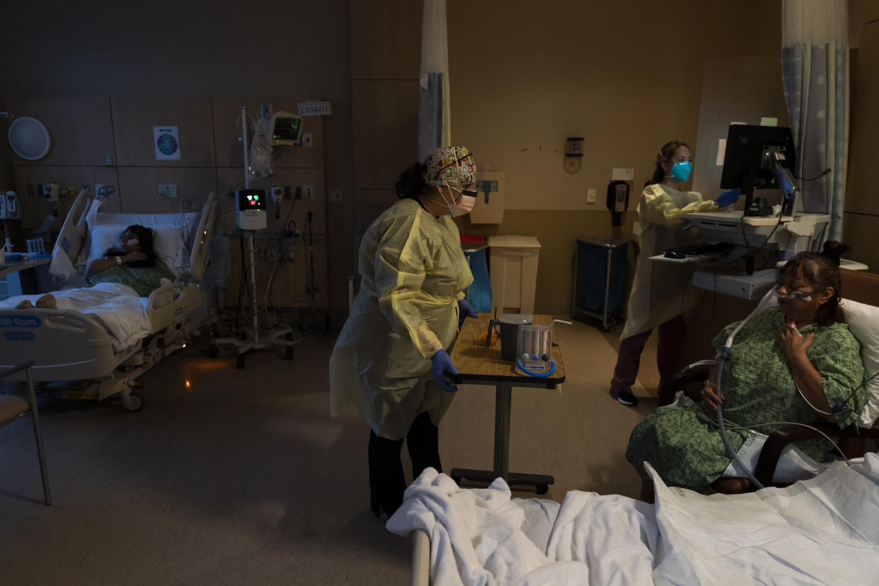 Registered nurse Nvard Termendzhyan, center, sets up a table for Linda Calderon, right, as her twin sister Natalie Balli, far left, rests in her bed in a COVID-19 unit at Providence Holy Cross Medical Center in Los Angeles, Monday, Dec. 13, 2021. The sisters were admitted to the hospital on the same day, a few days after their Thanksgiving gathering. (AP Photo/Jae C. Hong)