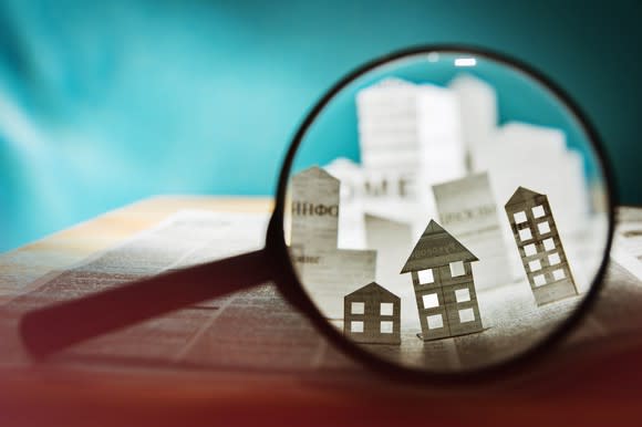 Magnifying glass looking at paper pop-up buildings.