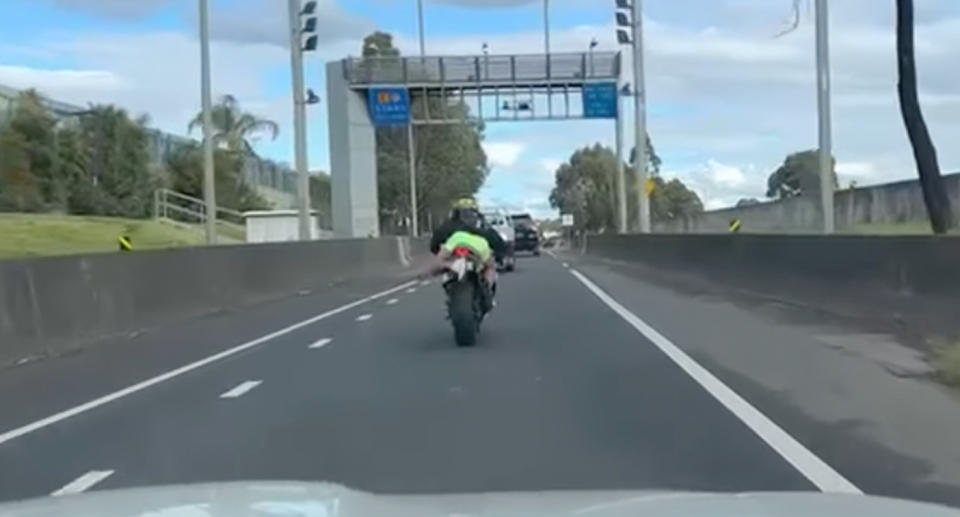 A photo of a motorcyclist trying to avoid paying a toll on an Australian road by propping his foot up to cover his licence plate.