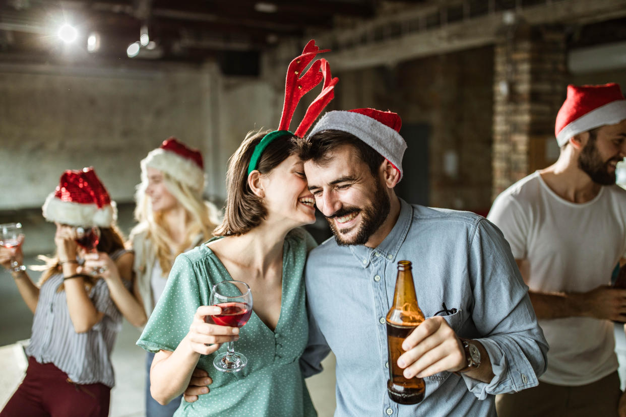 Young happy couple having fun while whispering on New Year's party at casual office.