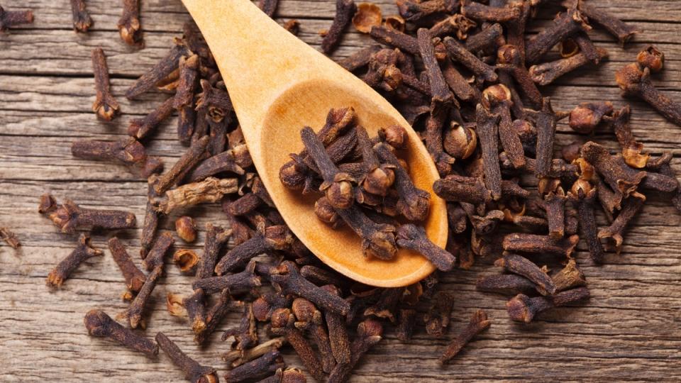 Cloves in a wooden spoon on a wood table