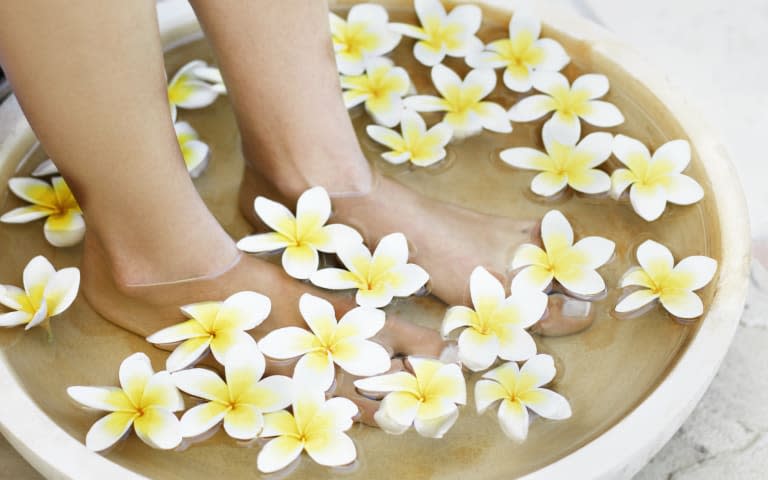 A woman's feet soaking in a bowl of water and flowers