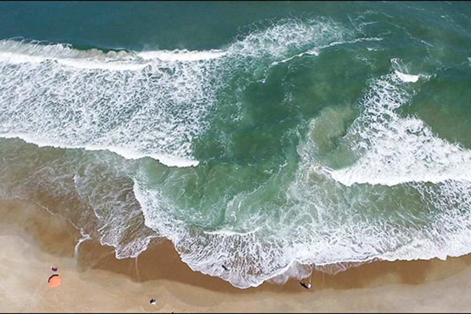 Aerial view of a wave hitting the shore, forming an isolated pool in the middle of the wave (NOAA)