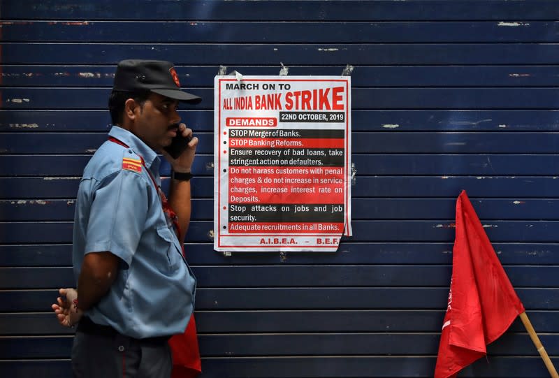 A private security guard speaks in front of a closed Kotak Mahindra Bank branch during a day-long strike against mergers of several state-run banks, in Kolkata,
