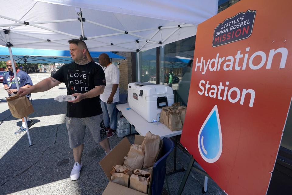 Carlos Ramos hands out bottles of water and sack lunches as he works at a hydration station in front of the Union Gospel Mission in Seattle.